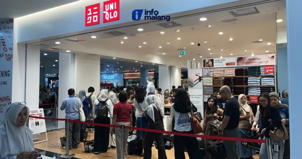 Pengunjung mengantre di balik tali pembatas merah di depan pintu masuk gerai Uniqlo, Lantai 2 Mall Olympic Garden Malang, dengan rak sweater di sisi kanan.